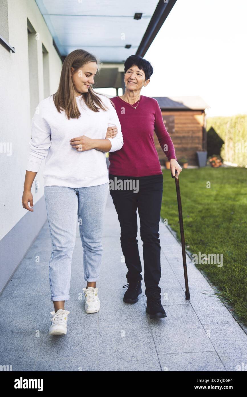 Junge kaukasische Frau, Krankenschwester, bei einem Hausbesuch, um eine Seniorin zu versorgen. Die Schwester hilft einer Seniorin bei den täglichen Aufgaben, hilft ihr, zu laufen Stockfoto