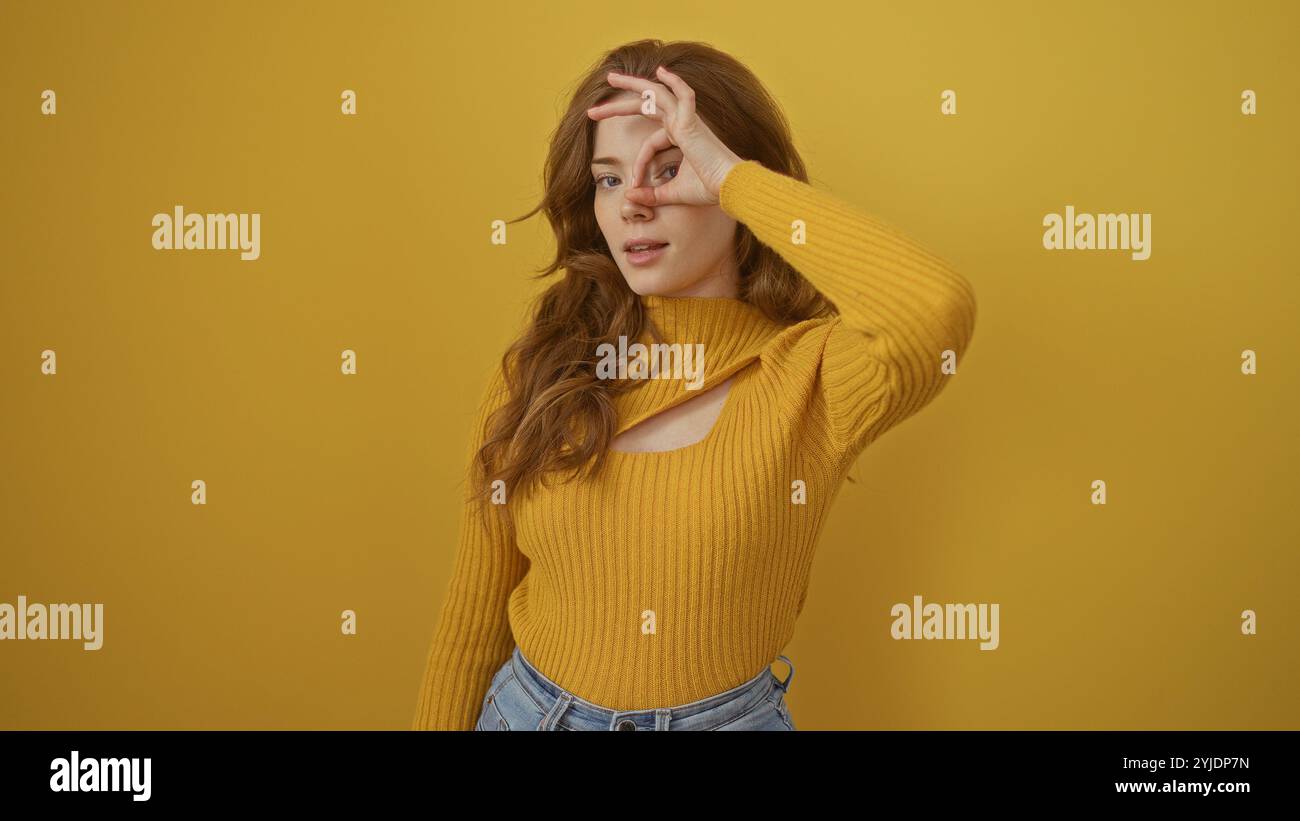 Eine schöne junge Frau mit blondem Haar macht eine gute Geste vor ihrem Auge, während sie vor einer gelben isolierten Hintergrundwand steht. Stockfoto