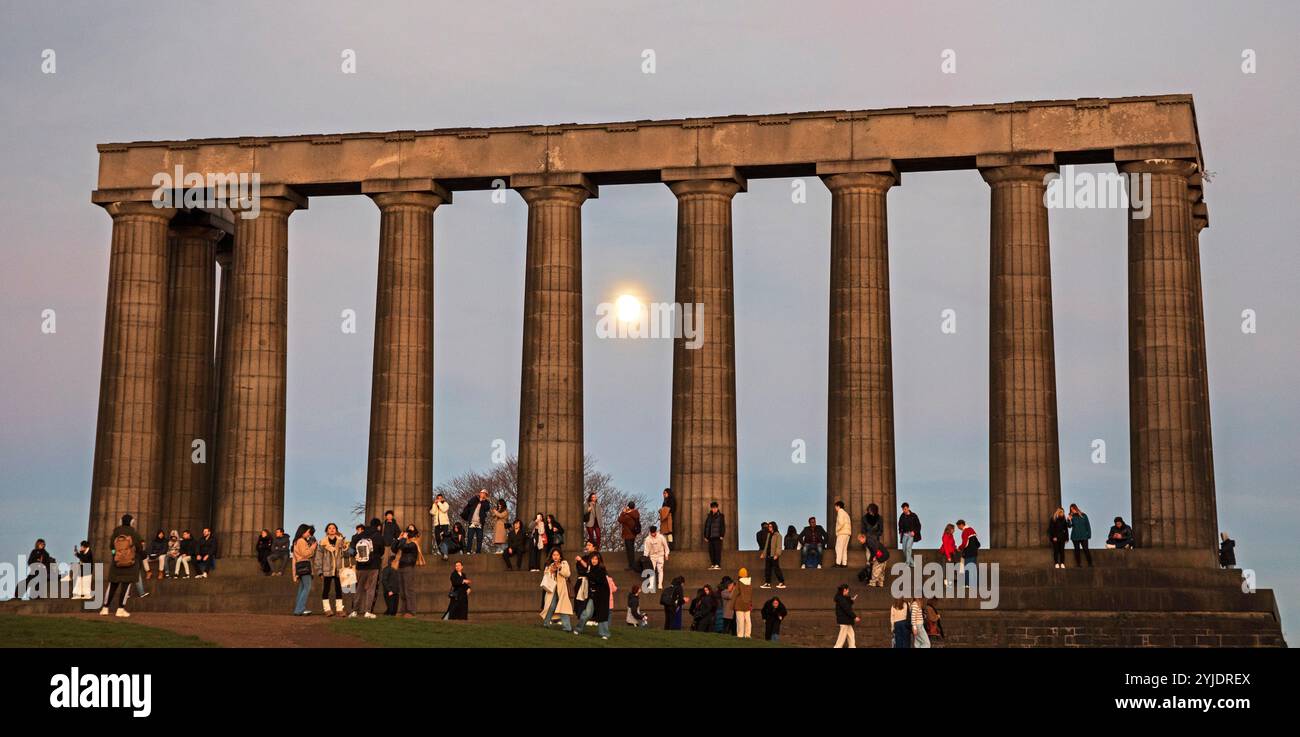 Calton Hill, Edinburgh, Schottland, Großbritannien. November 2024. Touristen treffen sich am malerischen Aussichtspunkt im Stadtzentrum, um den Sonnenuntergang zu beobachten und sie haben den Vollmond als Bonus bekommen. Temperatur leicht 12 Grad Celsius. Im Bild: Touristen schwärmen überall im National Monument und machen Selfies. Mit dem neuen vollen Bibermond im Hintergrund. Hinweis: Am Freitagabend erscheint der supermond. Der volle Beaver Moon steigt am 15. November um 15:30 Uhr GMT in Großbritannien auf und markiert das Ende einer Reihe von vier aufeinanderfolgenden Supermonden. Es werden Live-Nachrichten von Archwhite/Alamy veröffentlicht. Stockfoto