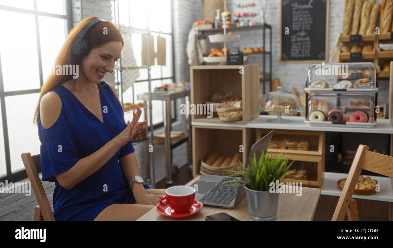 Frau, die während einer Videokonferenz in einer gemütlichen Bäckerei mit verschiedenen Backwaren auf einem Laptop spricht Stockfoto