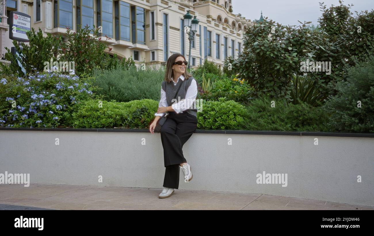 Frau lächelt im Freien in monaco, umgeben von üppigem Grün und eleganter Architektur, die eine ruhige und luxuriöse Atmosphäre darstellt. Stockfoto