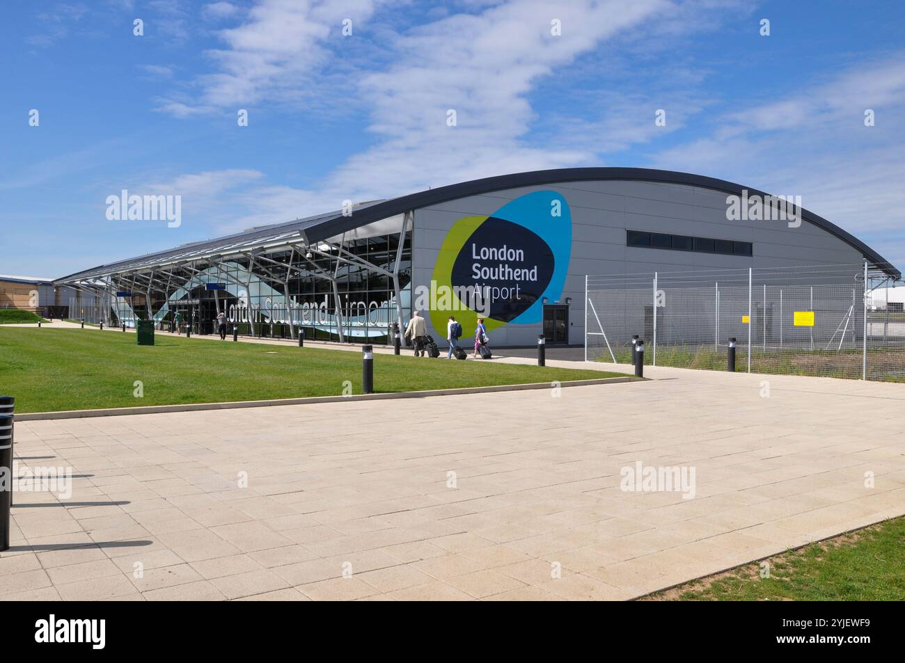 Flughafen London Southend. Passagiere mit Gepäck, die in Richtung des Terminalgebäudes fahren, mit dem London Southend Airport Logo und dem Symbol Stockfoto