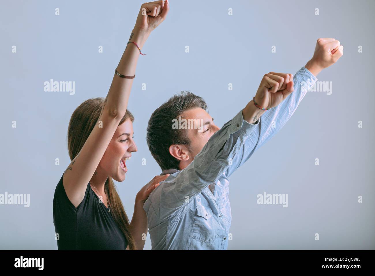 Das Paar hebt die Arme zur Feier und drückt pure Begeisterung aus. Der enthusiastische Beifall der Frau und die freudige Haltung des Mannes stellen Einheit und Einheit dar Stockfoto