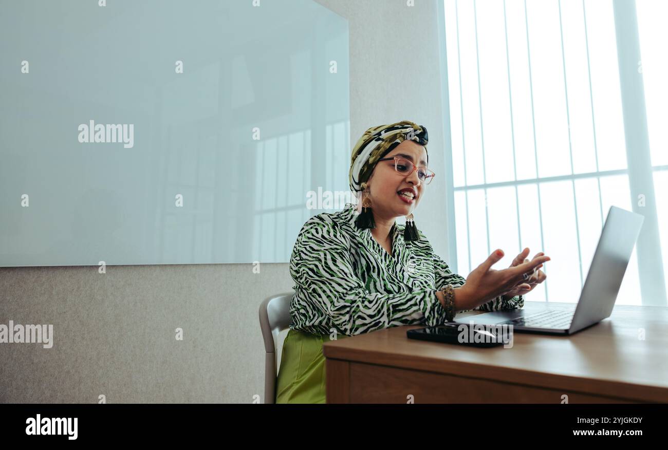 Indische Geschäftsfrau engagiert sich leidenschaftlich an einem virtuellen Geschäftstreffen von einem modernen Büro aus. Ihre ausdrucksstarken Gesten heben die effektive Arbeit hervor Stockfoto