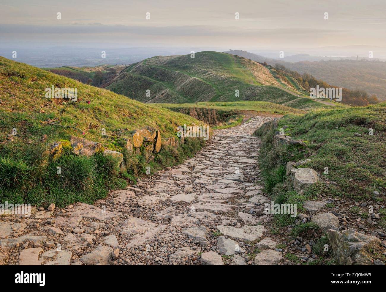 Eine alte steinzeitliche Festung in den Malvern Hills, Großbritannien, mit Landschaft in der Ferne. Ein Steinweg im Vordergrund führt das Auge zur Mitte des Bodens Stockfoto