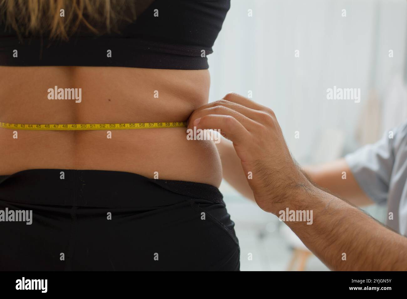 Medizinische Ernährungsberaterin in einem grauen Hemd misst die Taille einer Frau mit einem Maßband. Nahaufnahme. Stockfoto