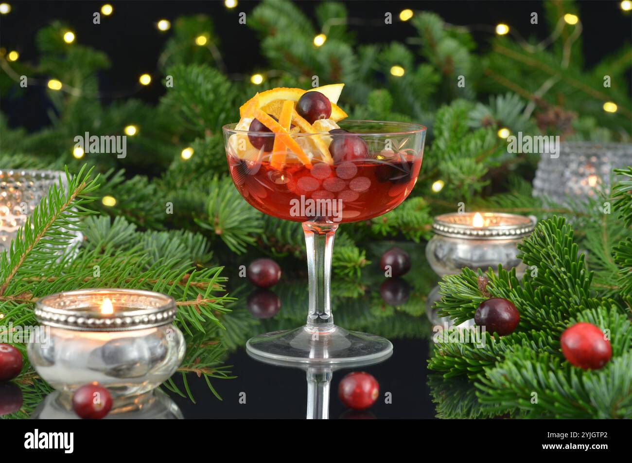 Silvestergetränk in einem Glas mit Lichtern, brennenden Kerzen und grünen Zweigen auf dunklem Hintergrund. Stockfoto