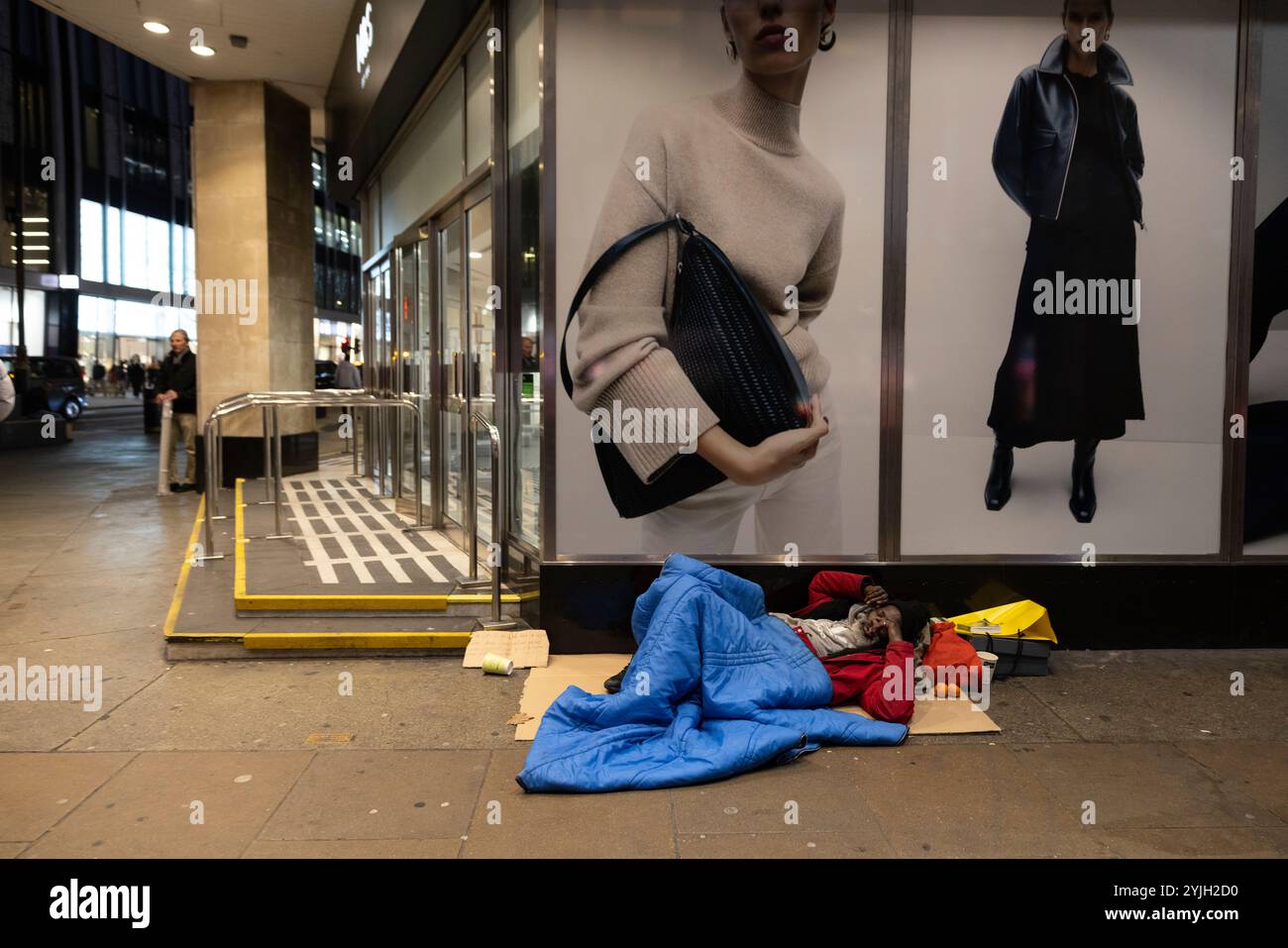 Obdachloser Mann schläft unter einer Damenmodewerbung vor Marks & Spencers Marble Arch Flagship Store im Zentrum von London, England, Großbritannien Stockfoto