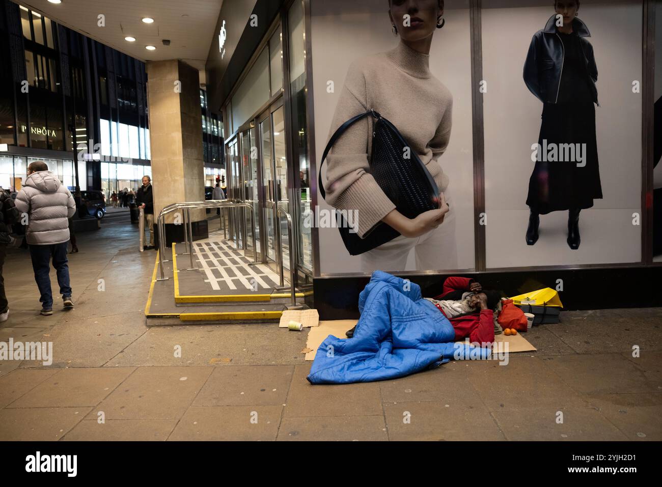 Obdachloser Mann schläft unter einer Damenmodewerbung vor Marks & Spencers Marble Arch Flagship Store im Zentrum von London, England, Großbritannien Stockfoto