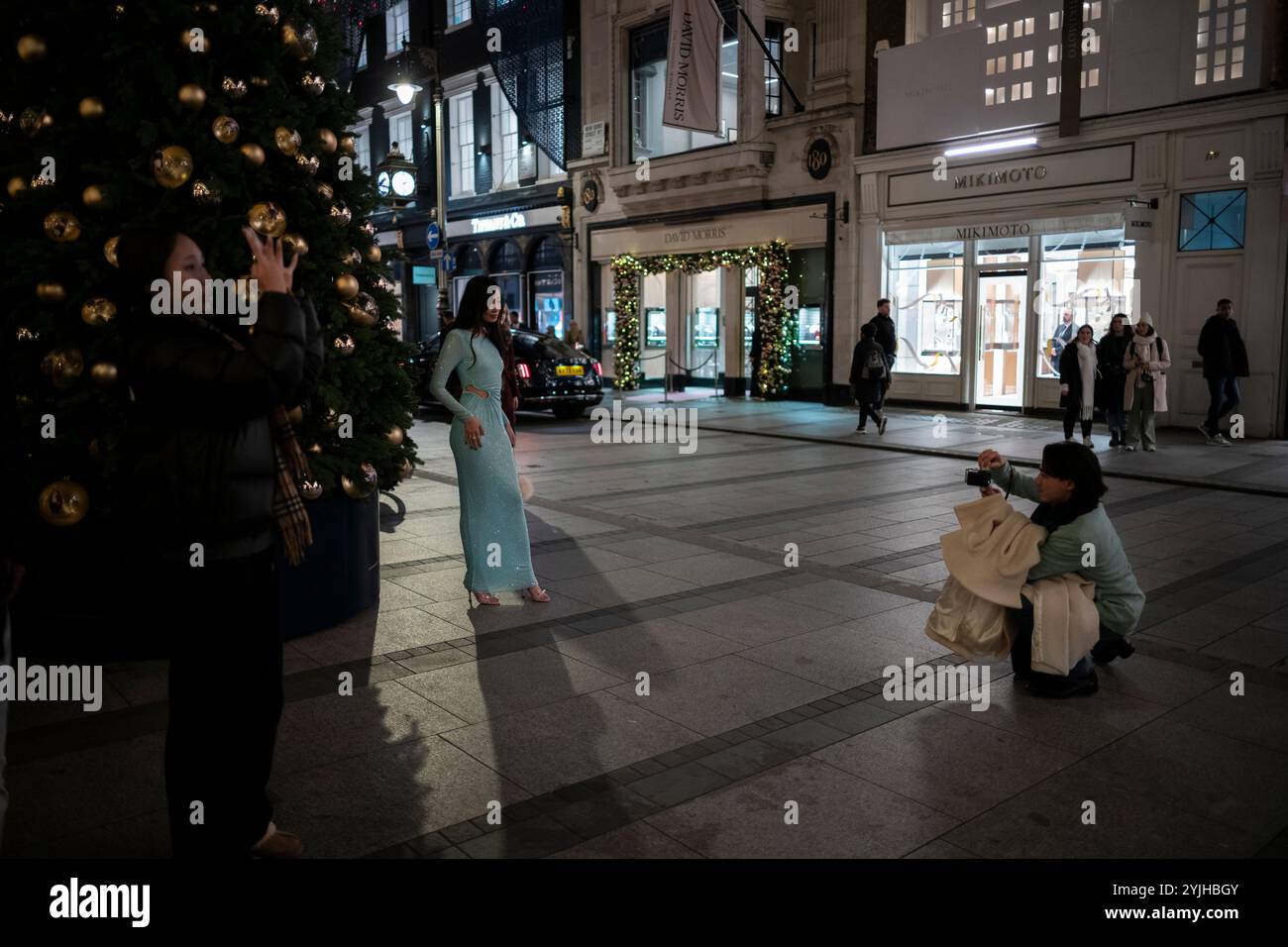 Touristen halten an und machen Fotos von den Weihnachtsfenstern und Weihnachtslichtern entlang der Old Bond Street, Mayfair, im Zentrum von London, England, Großbritannien Stockfoto