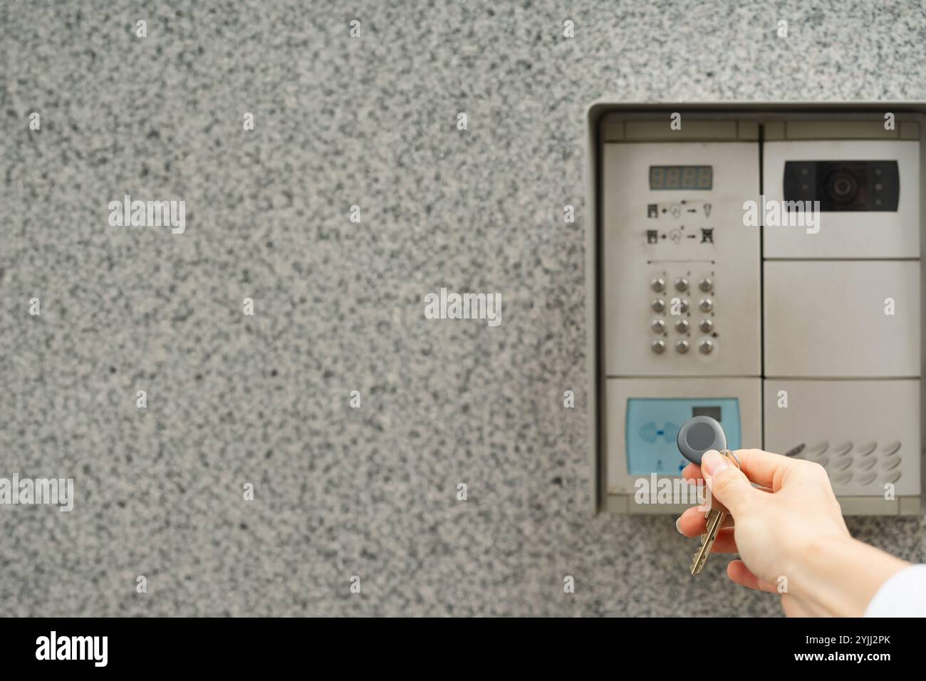 Frauenhand mit Schlüsselanhänger gegen Gegensprechanlage Stockfoto