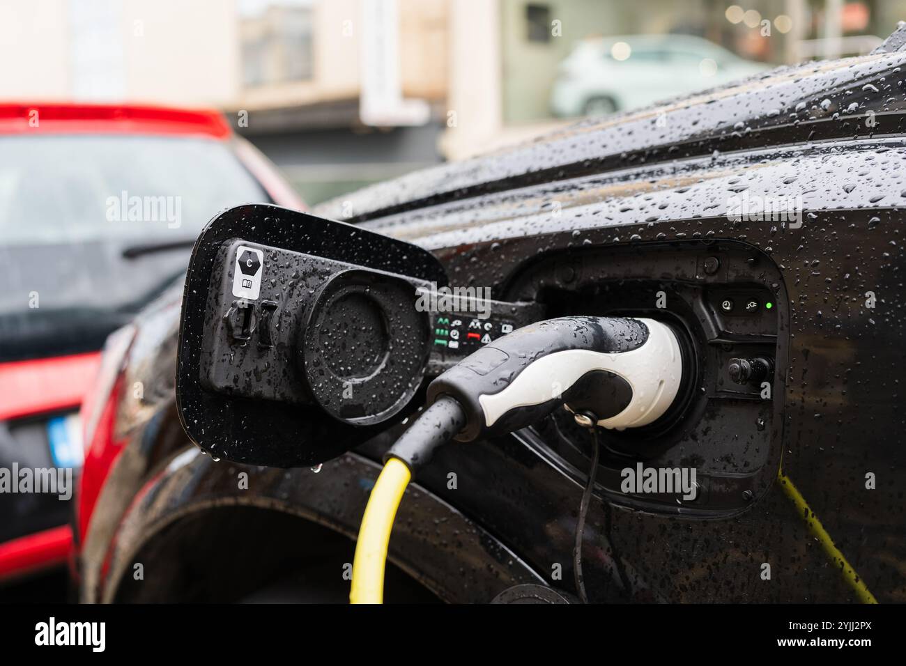 Elektrostecker, der das Auto an regnerischem Tag auflädt Stockfoto