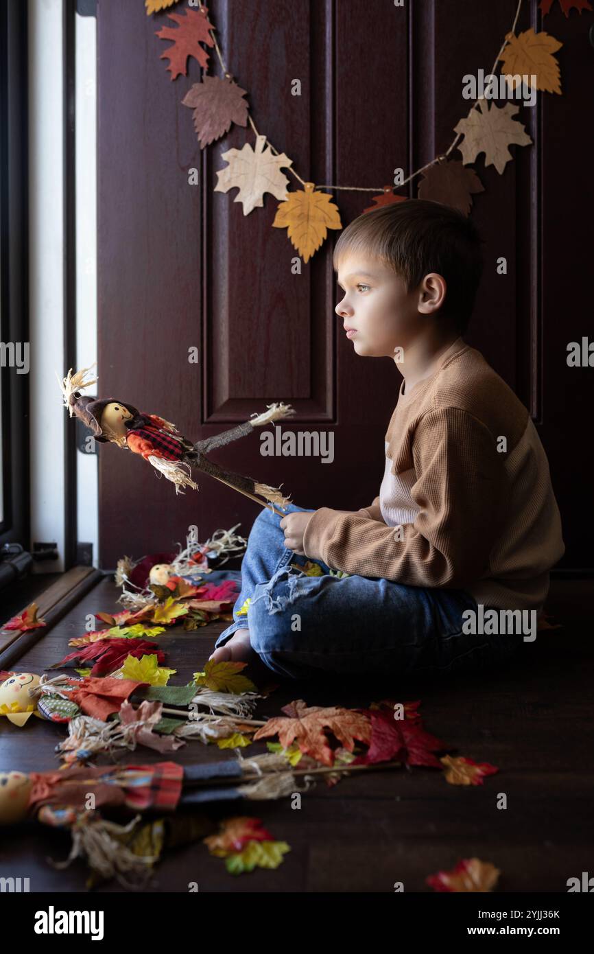 Junge, der an der Tür sitzt und mit Spielzeugscheuchen spielt Stockfoto