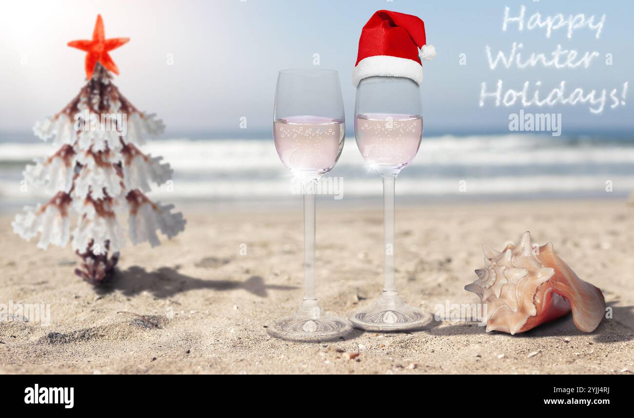 Feiern Sie die Winterferien mit einem einzigartigen Korallenweihnachtsbaum, zwei prickelnden Drinks mit einem Weihnachtsmann-Hut, vor einer warmen Strandkulisse Stockfoto