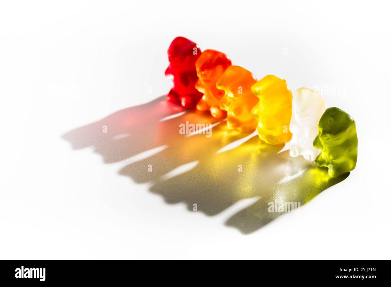 Eine Reihe von bunten Gummibären auf weißem Hintergrund, die lebendige Schatten erzeugen Stockfoto