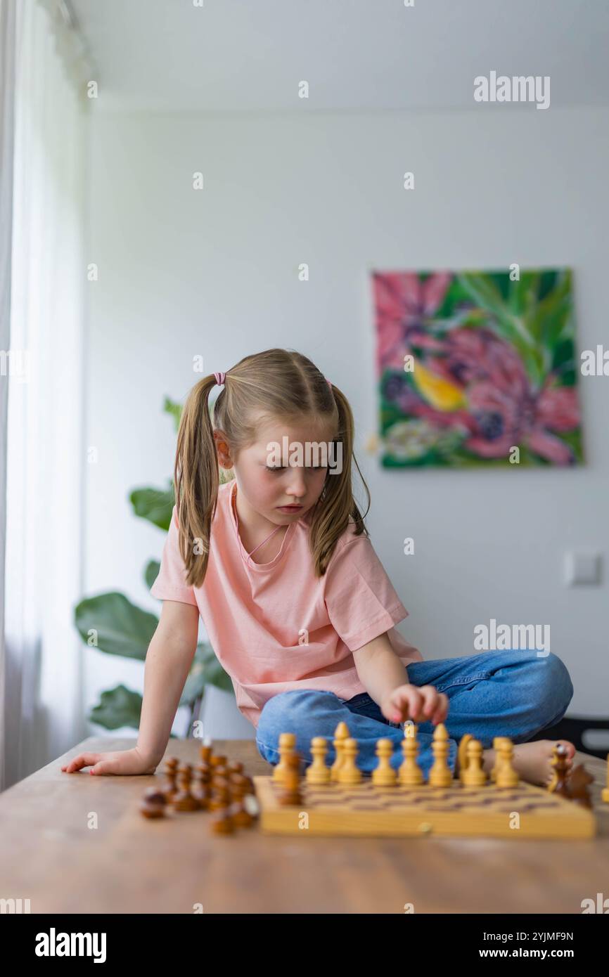 Ein junges Mädchen, 5 Jahre alt, spielt Minischach und plant ihren nächsten Zug mit Sorgfalt in einem spielerischen Lernmoment. Hochwertige Fotos Stockfoto