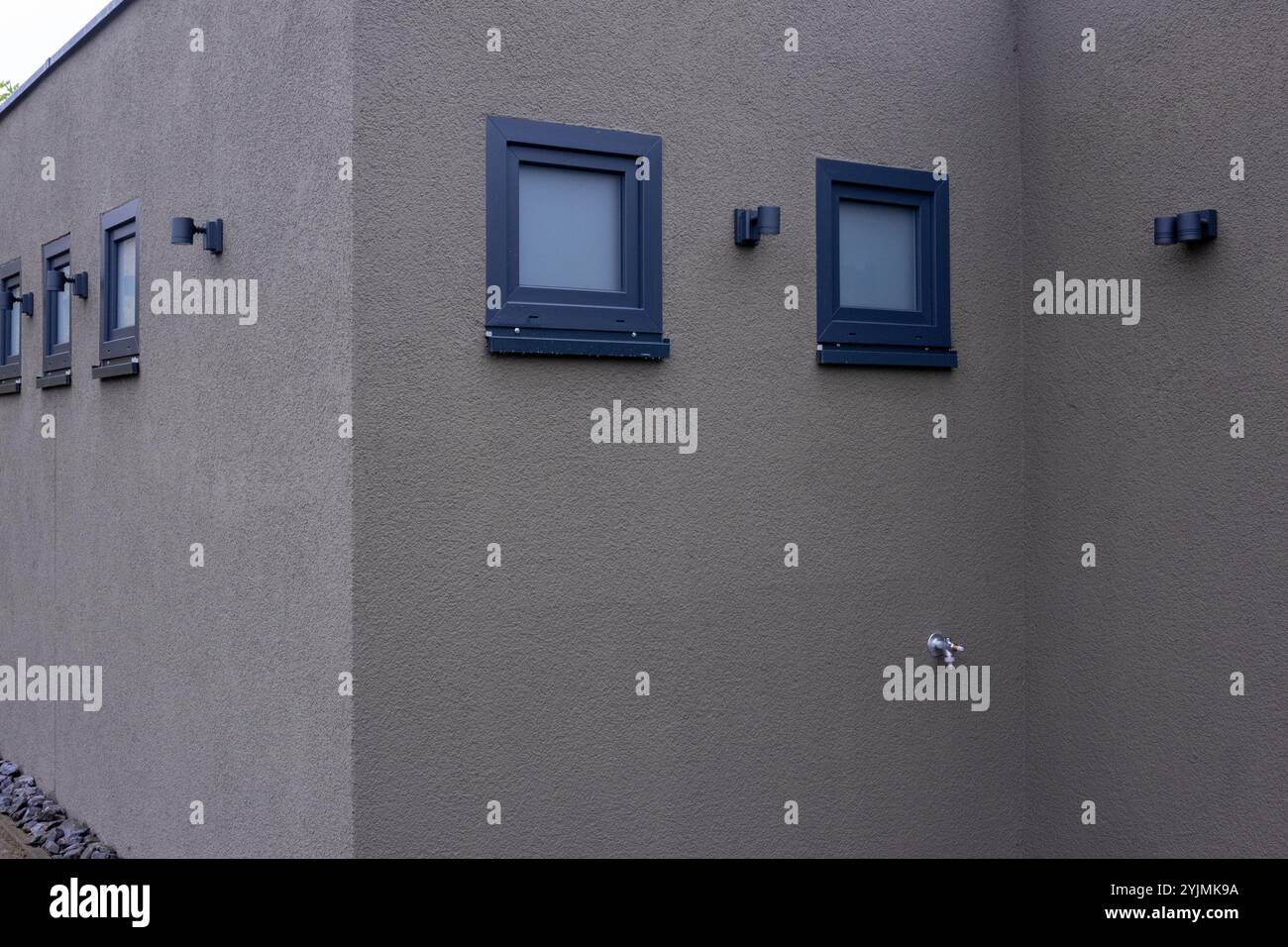 Modernes Haus mit Putzwänden, dunkel gerahmten Fenstern und Außenbeleuchtung Stockfoto