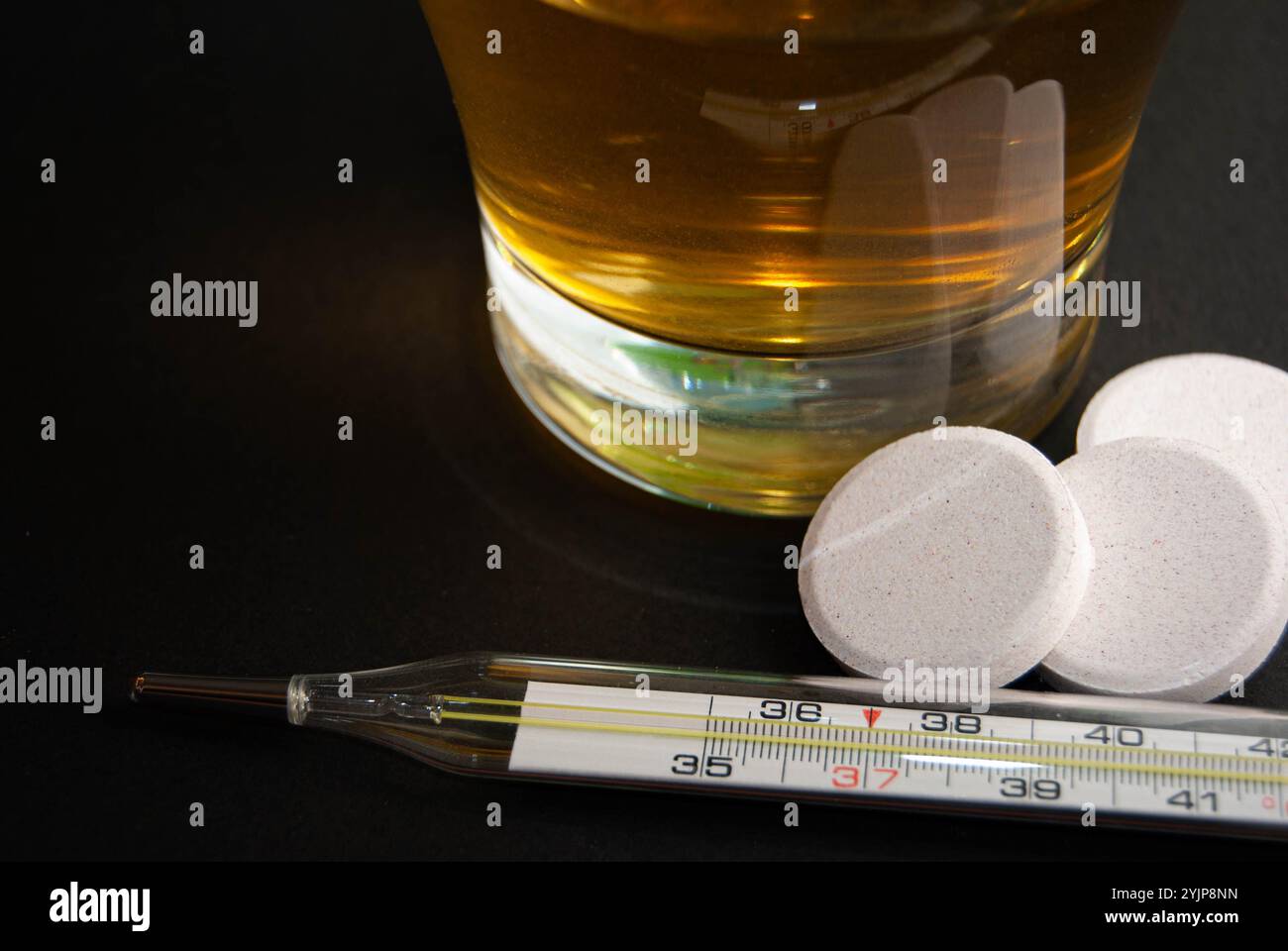 Kräuterkamillentee neben Thermometer und Brausetabletten vor dunkler Kulisse, symbolisiert Wellness, Gesundheit und Grippelinderung. Stockfoto