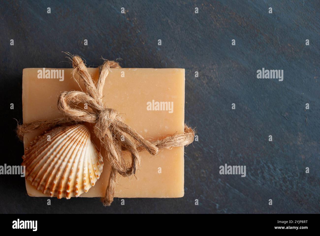 Hausgemachte Lavendelseife mit dekorativer Schleife und Muscheln auf dunklem Hintergrund für eine beruhigende, natürliche Szene. Stockfoto