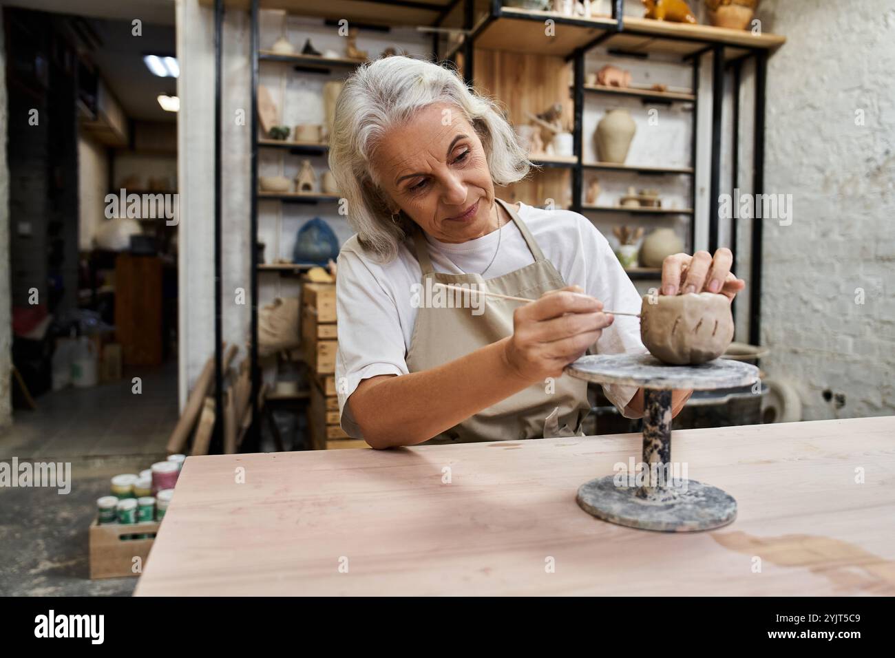 Eine talentierte, reife Frau konzentriert sich darauf, in ihrer Werkstatt ein einzigartiges Töpferwerk zu Formen. Stockfoto