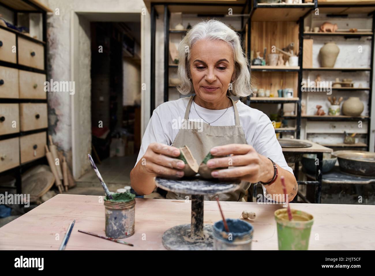 Eine talentierte, reife Frau formt sorgfältig Ton und taucht in ihre kreative Töpferstunde ein. Stockfoto