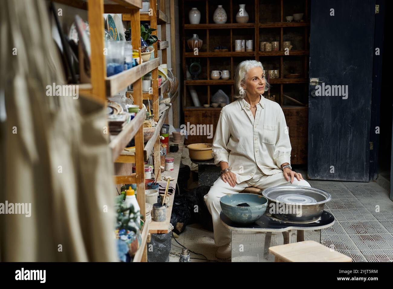 Eine elegante, reife Frau konzentriert sich auf ihre Töpferei in einem gut organisierten Studio-Raum. Stockfoto