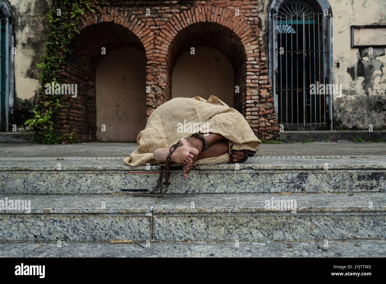 Schwarze Frau, verkleidet als Sklave in Ketten, liegt auf der Treppe einer Straße in Pelourinho. Sklaverei in Brasilien. Darstellung der Sklaven Anastacia. Stockfoto
