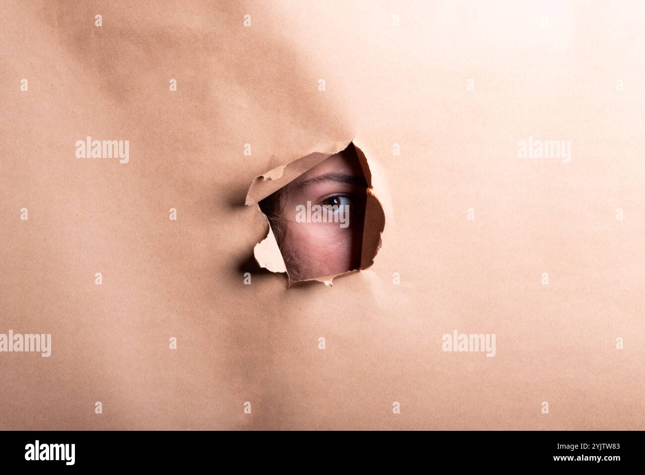 Das Auge eines Mannes, der durch ein Loch in einem Blatt Papier schaut. Studio-Porträt. Stockfoto