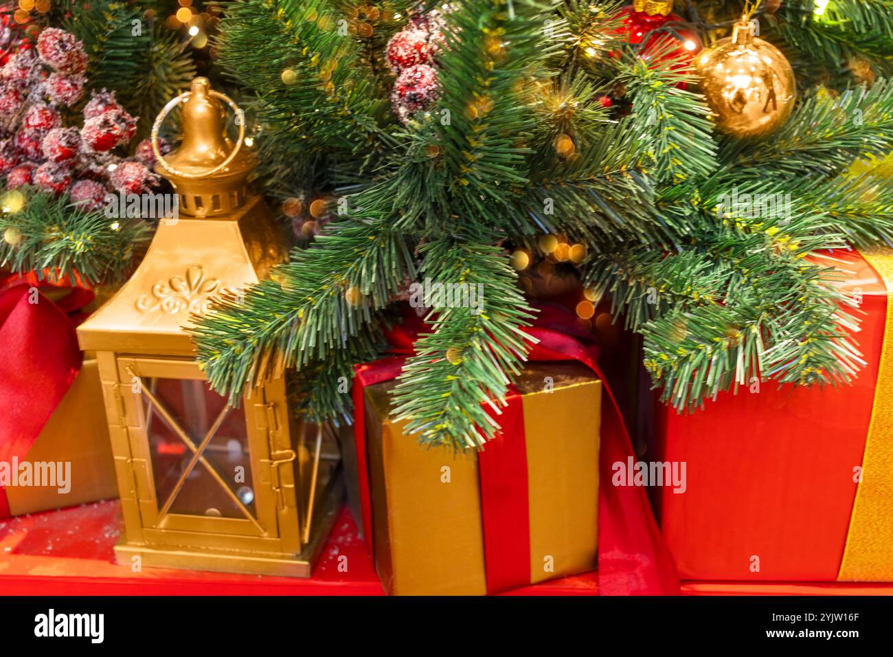 Goldene Laterne und Geschenke unter dem Weihnachtsbaum, dekoriert mit Ball und roten Beeren. Stockfoto