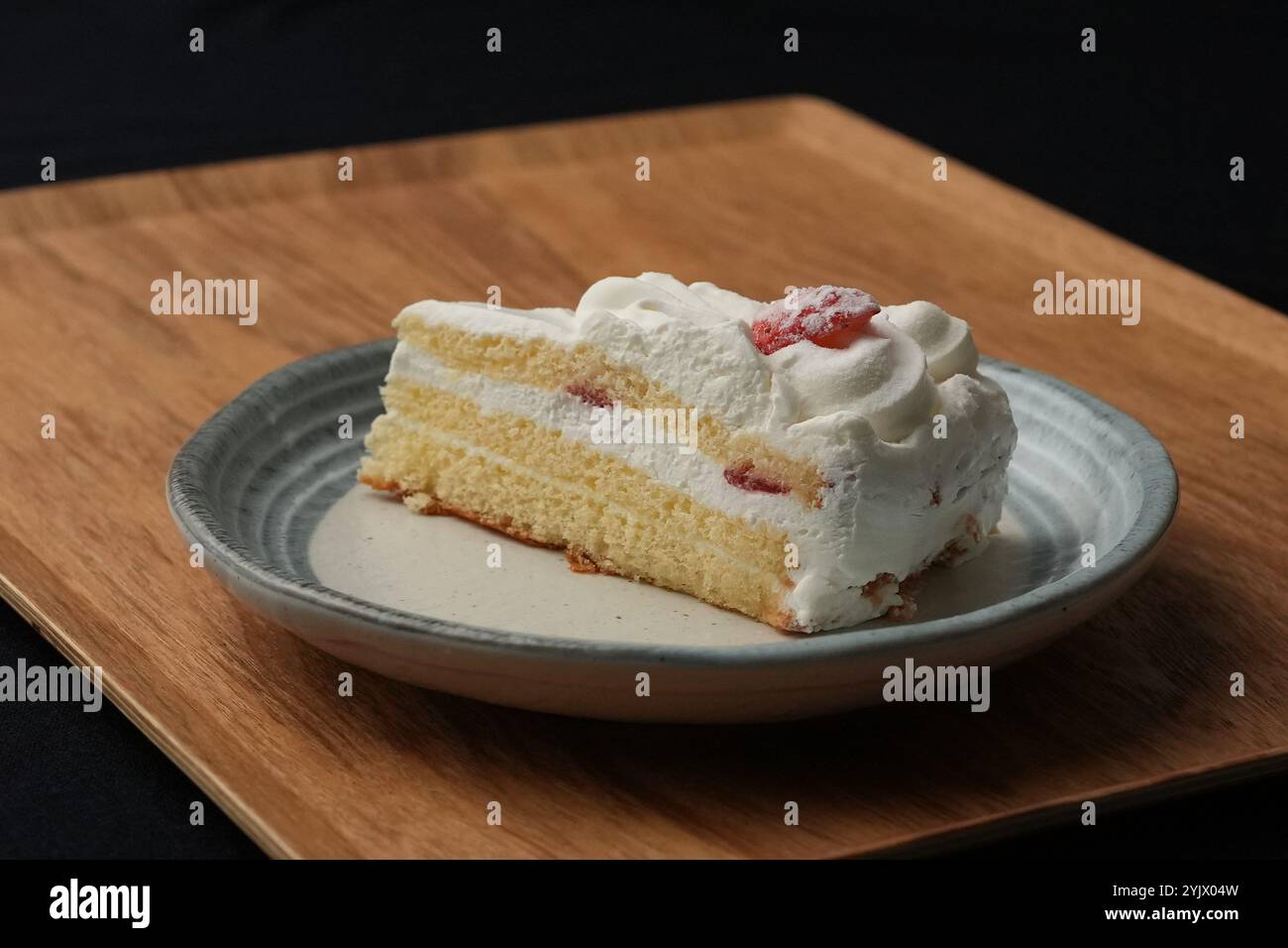 Ein kleiner japanischer Erdbeerkuchen auf einem stilvollen japanischen Teller auf einem Holztablett auf einem schwarzen Tuch auf einem weißen Tisch. Stockfoto