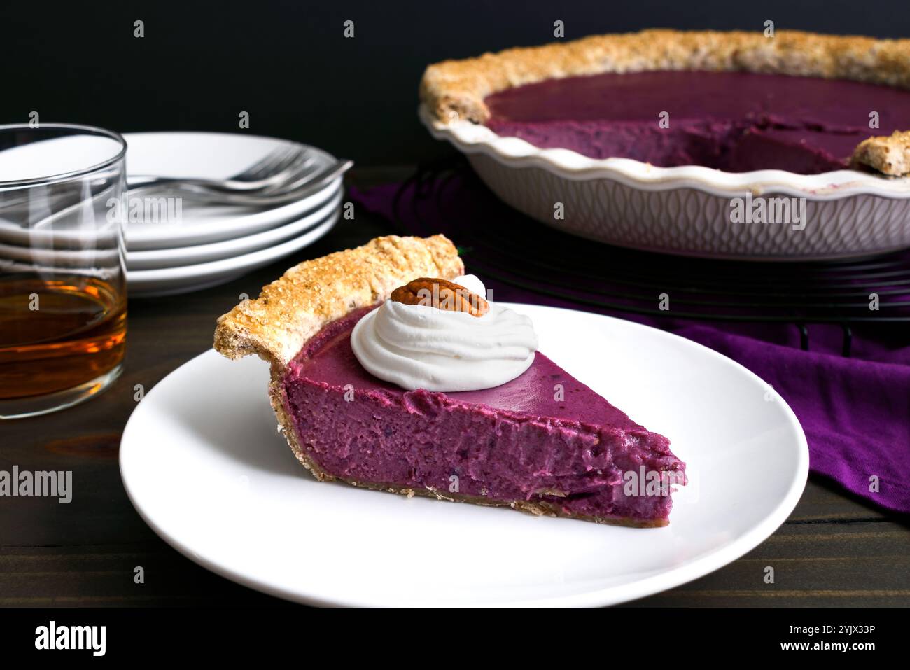 Ein Stück Purple Sweet Potato Pie mit Schlagsahne und einem Pecan: Seitenansicht eines hausgemachten lila Süßkartoffeltortes mit einem Glas Bourbon Stockfoto