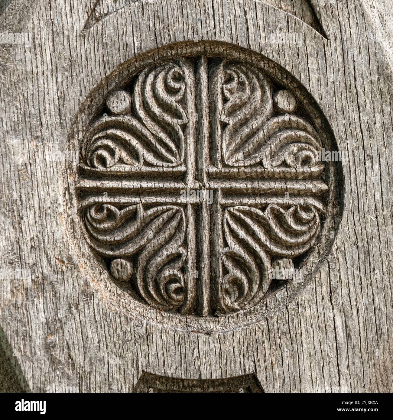 Nahaufnahme eines detaillierten kreisförmigen Kreuzes, das in verwittertes Holz geschnitzt wurde, mit verzierten Wirbeln und veralteter Textur, die Erbe und Handwerkskunst symbolisieren. Stockfoto