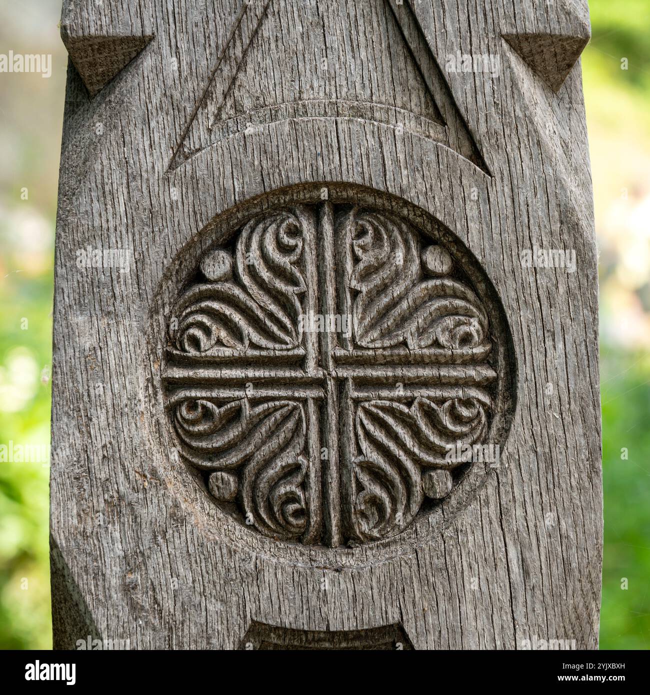 Nahaufnahme eines rustikalen Holzkreuzes mit komplizierten Wirbeln und kreisförmigem Design, das Handwerkskunst und religiöser Symbolik betont, vor einem natürlichen Hintergrund Stockfoto