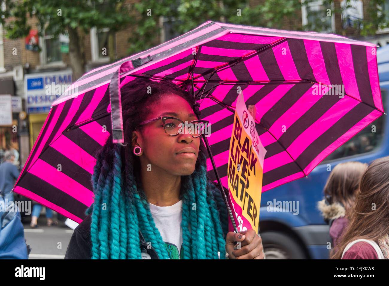 London, Großbritannien. Juli 2017. Eine Frau mit einem rosa gestreiften Regenschirm hält ein Black Lives Matter-Plakat vor der Stoke Newington Polizeistation für Rashan Charles, der starb, als zwei Polizisten ihn mit Handschellen in einem Geschäft an der Kingsland Rd in den frühen Morgenstunden des Samstag, den 22. Juli, auf dem Boden festhielten. Seine Familie ist entschlossen, Antworten auf seinen Tod zu bekommen, aber sie fordert alle auf, innerhalb des Gesetzes zu handeln. Mitglieder der Familie Charles kamen zusammen mit der Familie Edson da Costa zu dem Protest, der nach der Verhaftung in East Ham im Juni starb. Die Demonstranten hielten Bilder der beiden Männer und Darren Cumberb Stockfoto