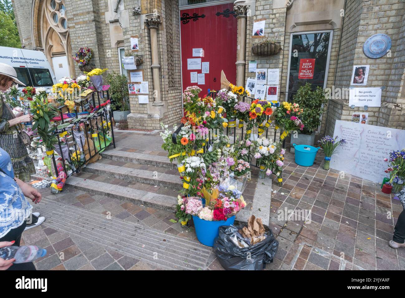 London, Großbritannien. Juni 2017. Plakate auf Lampenpfosten, Wänden und Pinnwänden zeigen die ergreifenden Bilder derjenigen, die beim verheerenden Brand im Turmblock fehlen, der mit brennbarem Material bekleidet war und keine funktionierende Feuermeldeanlage hatte. Der gesamte Bereich um den Turm ist noch abgesperrt, aber der grauschwarz verdunkelte Rumpf des Grenfell Tower dominiert. Außerhalb der Methodistenkirche wurde ein Bereich für Kerzen, Tribut und Blumen für die Toten und Vermissten, die jetzt als tot angesehen werden und deren Zahl heute auf über 150 geschätzt wird, reserviert. Stockfoto