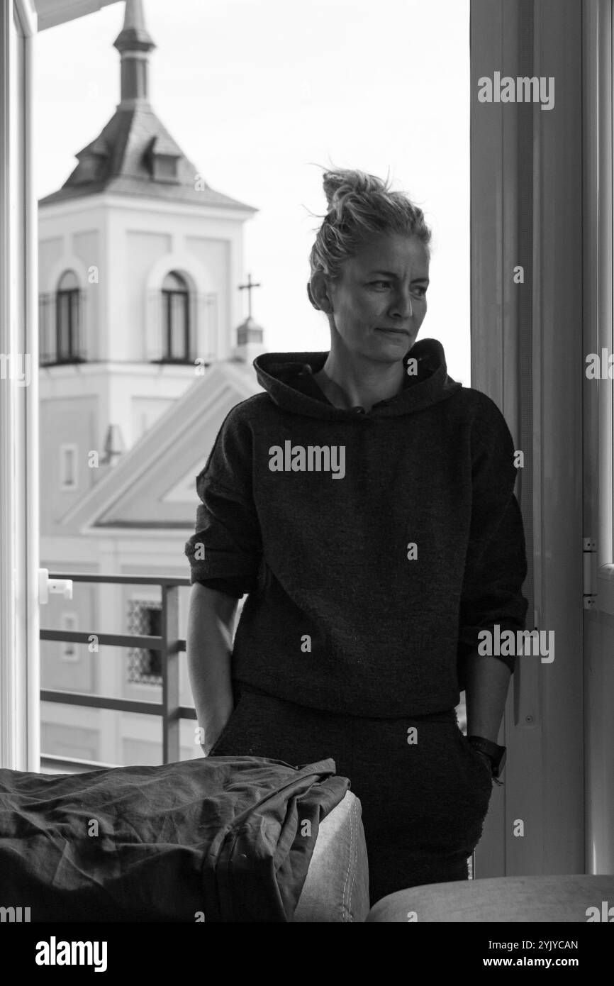 Blonde Frau mit Haaren in einem Trainingsanzug schaut durch das Fenster auf die Straße Stockfoto
