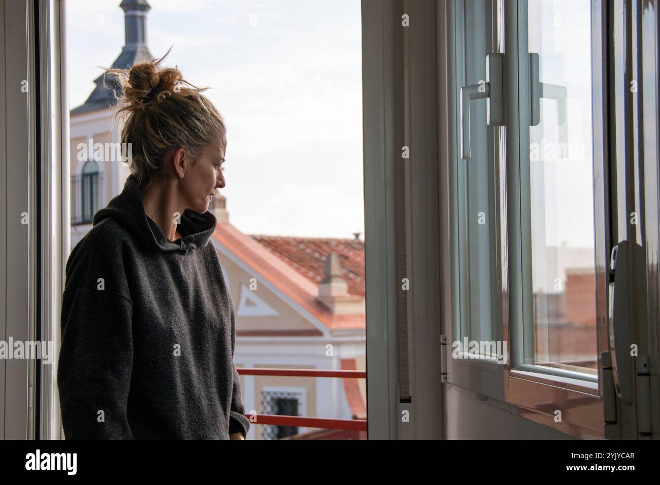 Blonde Frau mit Haaren in einem Trainingsanzug schaut durch das Fenster auf die Straße Stockfoto