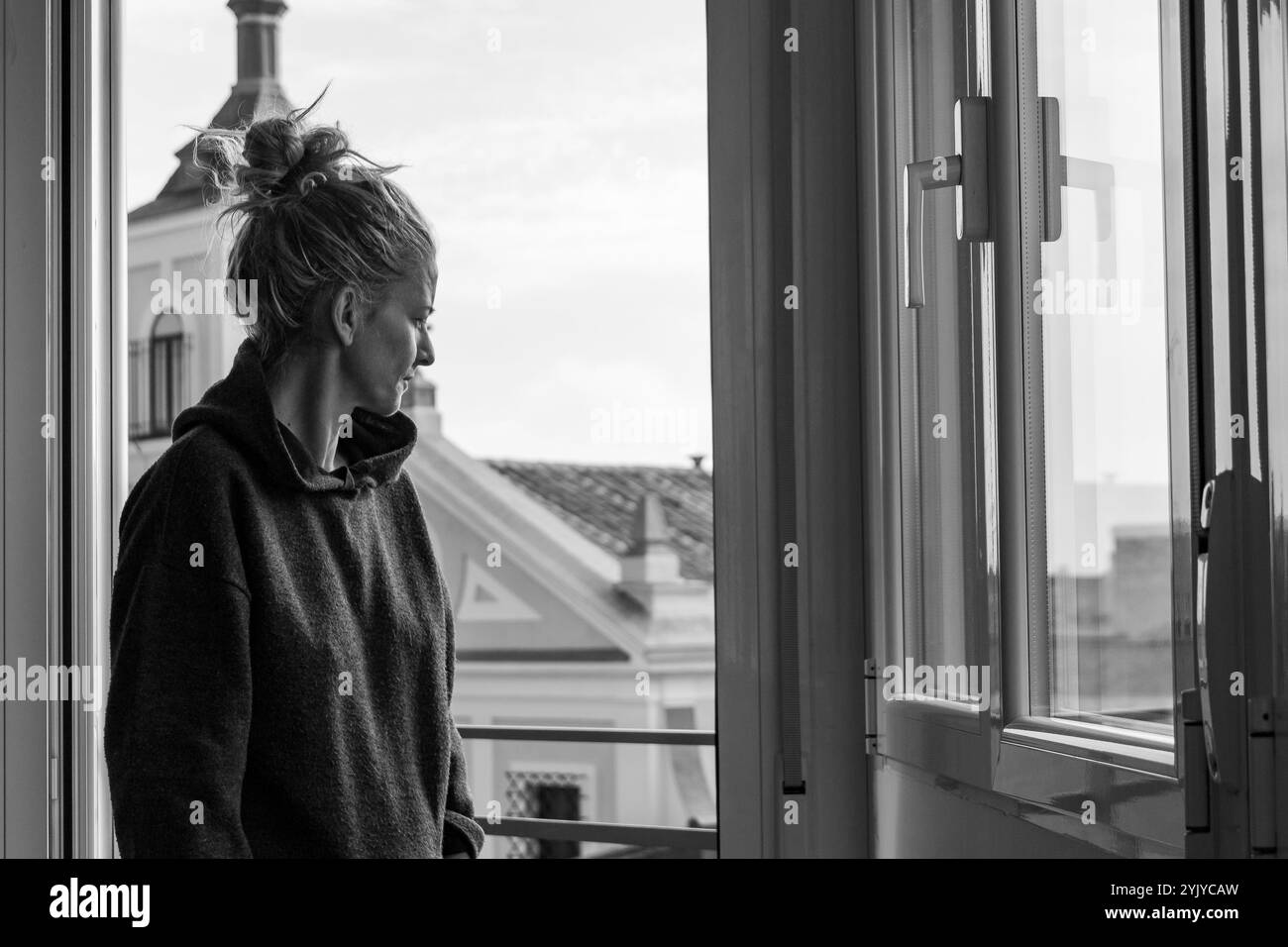 Blonde Frau mit Haaren in einem Trainingsanzug schaut durch das Fenster auf die Straße Stockfoto