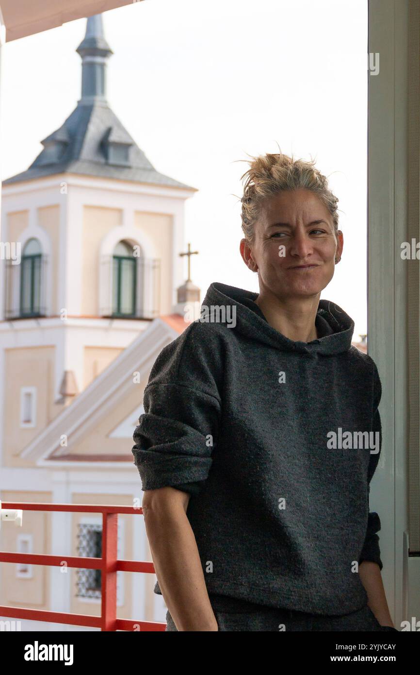 Blonde Frau mit Haaren in einem Trainingsanzug schaut durch das Fenster auf die Straße Stockfoto