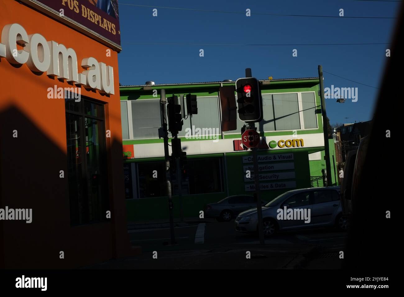 .com.au in großen Buchstaben auf einer hellorangen Wand eines Unternehmens, Detail der Typografie, ein anderes Geschäft, Ampeln, blauer Himmel, grüne .com, Autos Stockfoto