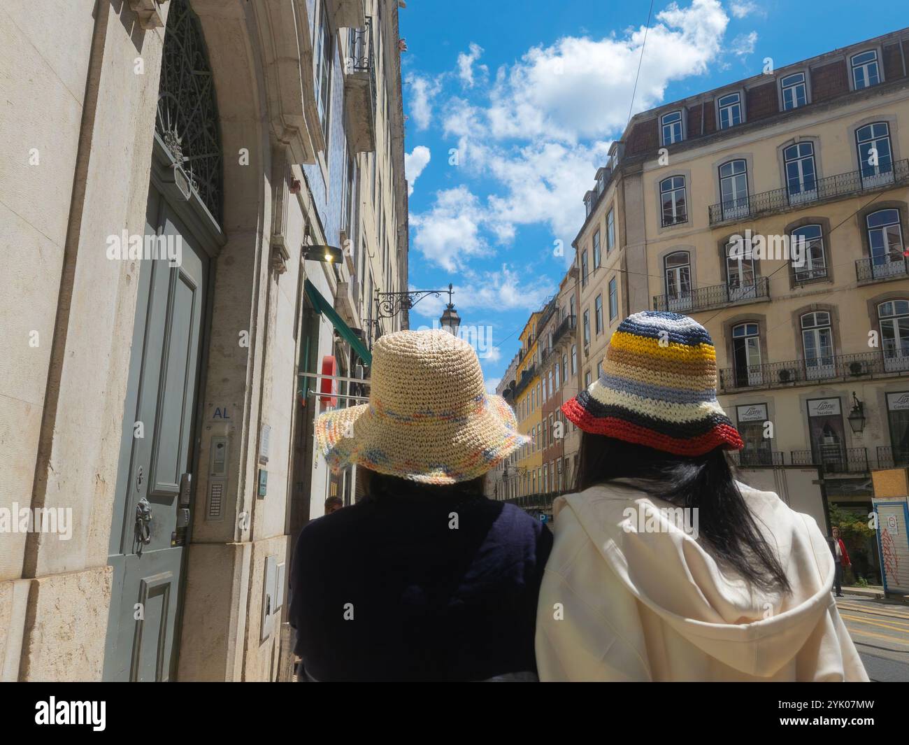 Lissabon, Portugal - an einem sonnigen Tag spazieren Touristen in bunten Hüten durch eine Straße in der Innenstadt mit alten Gebäuden, Rückansicht. Familienreisen in der Stadt - Smartphone-aufgenommenes Stockfoto