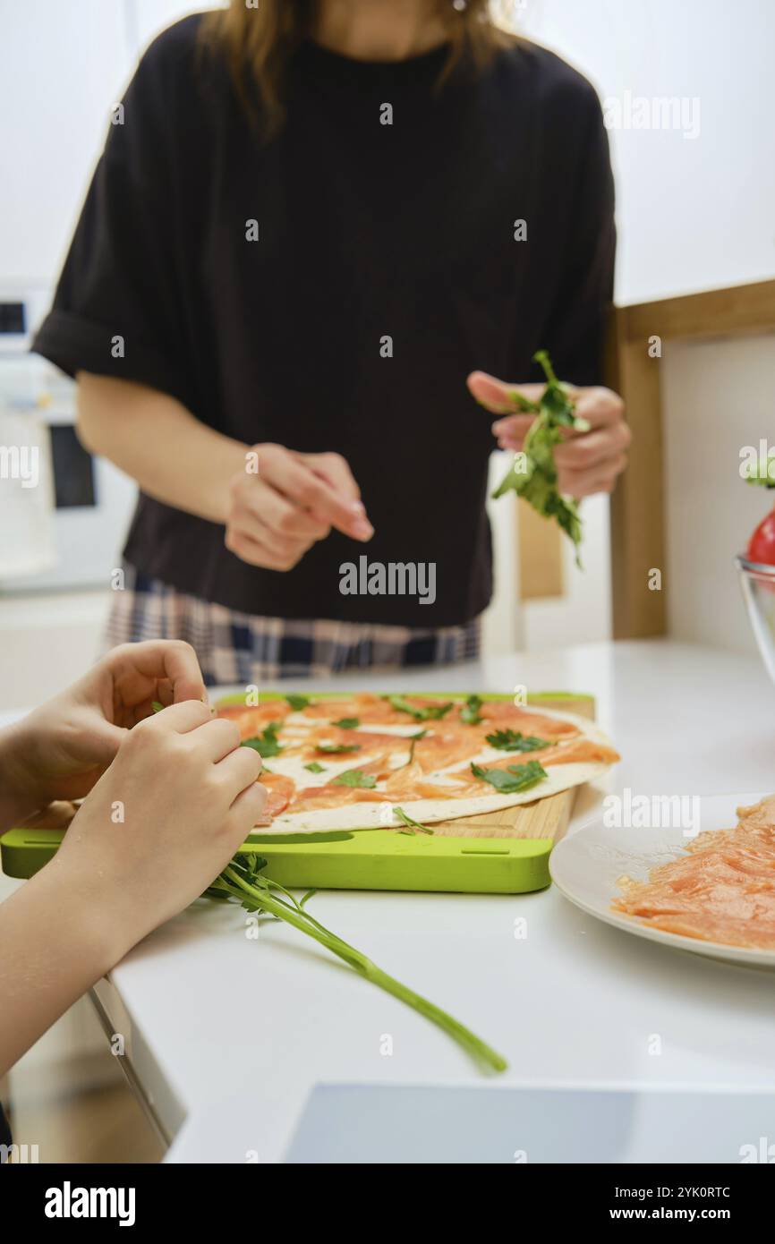 Nahaufnahme weiblicher Hände, die Petersilienblätter abreißen und auf Lachsapetizer legen Stockfoto