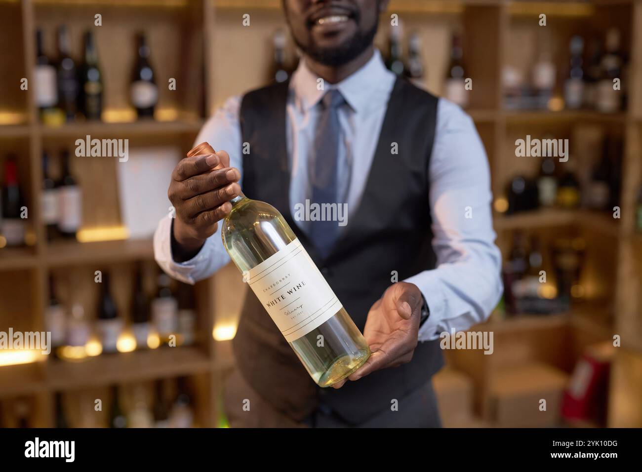 Mittlere Nahaufnahme einer exklusiven Weinflasche in den Händen eines nicht erkennbaren afroamerikanischen Sommeliers, der sie demonstriert Stockfoto