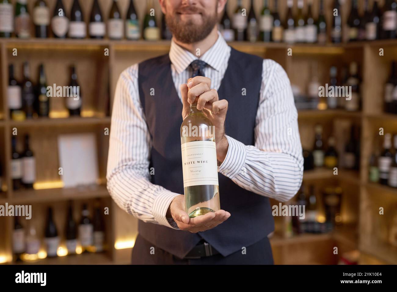 Mittlere Nahaufnahme eines nicht erkennbaren Sommeliers, der eine Flasche trockenen Weißweins in der Hand hält, während er für ein Foto posiert Stockfoto