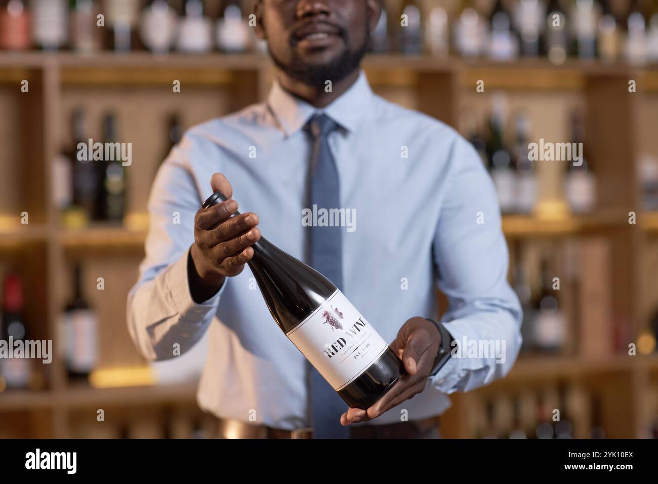 Mittlere Nahaufnahme der Rotweinflasche in nicht erkennbaren Sommelierhänden Stockfoto