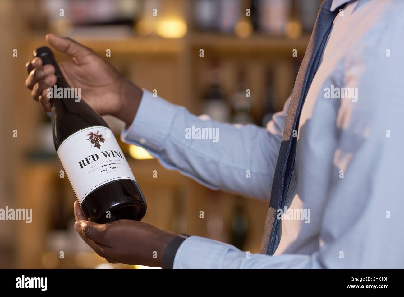 Mittlere Nahaufnahme einer dunklen Flasche Wein mit weißem Etikett in den Händen eines nicht erkennbaren Sommeliers Stockfoto