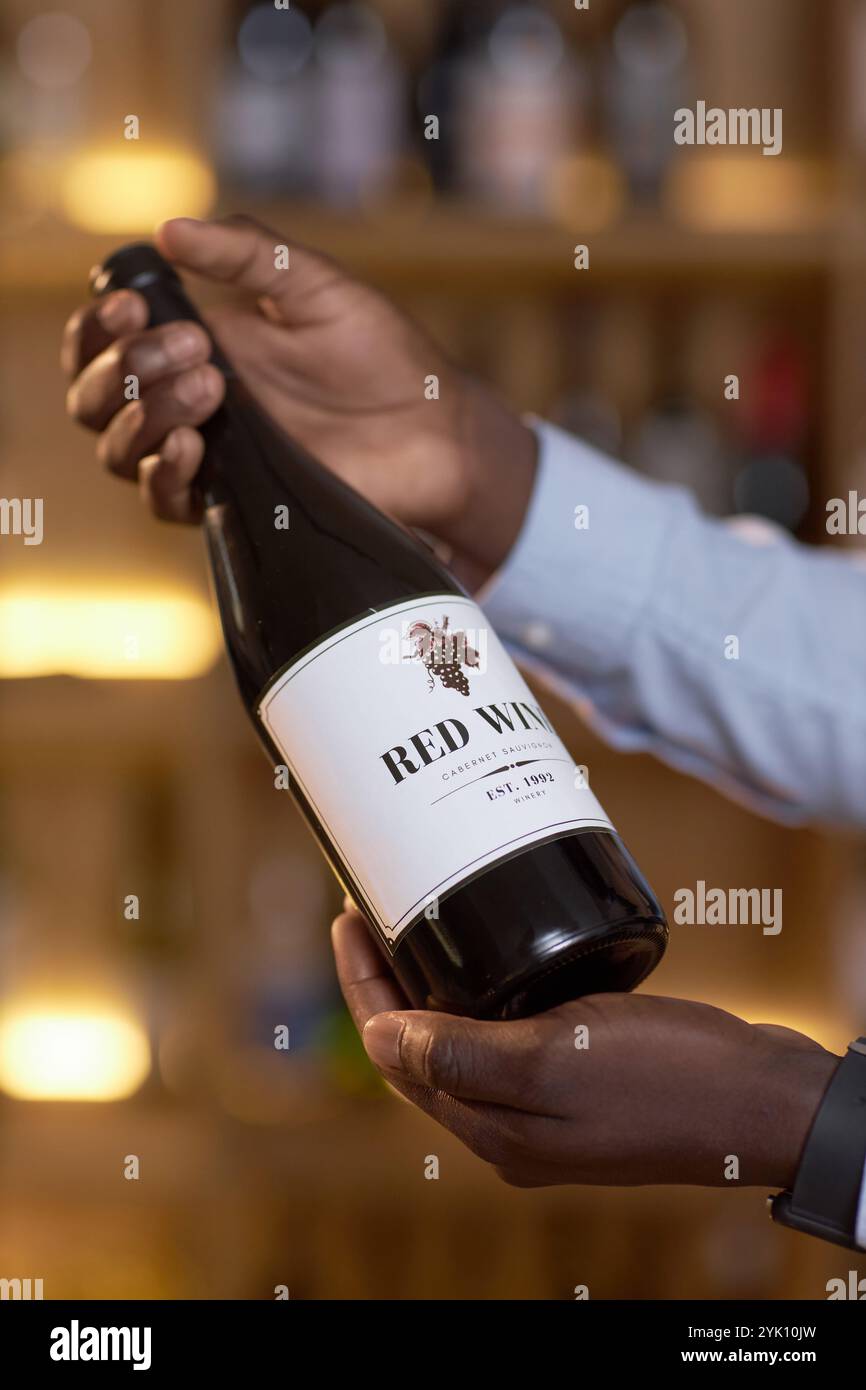 Vertikaler Schuss der Flasche mit weißem Etikett voll mit trockenem Rotwein in männlichen Händen Stockfoto