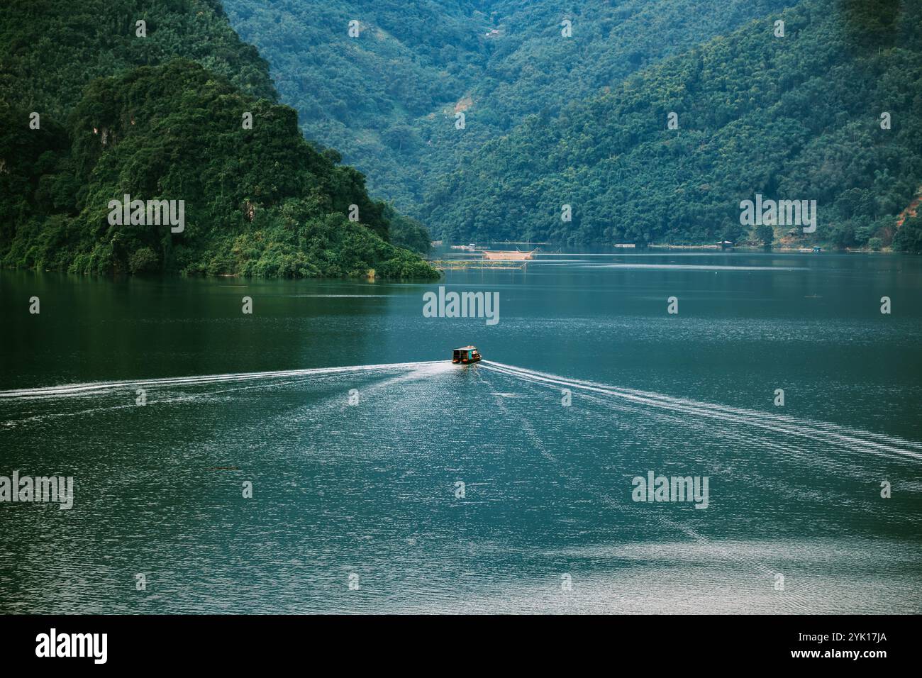 Boot auf einem ruhigen Fluss umgeben von üppigen grünen Hügeln Stockfoto