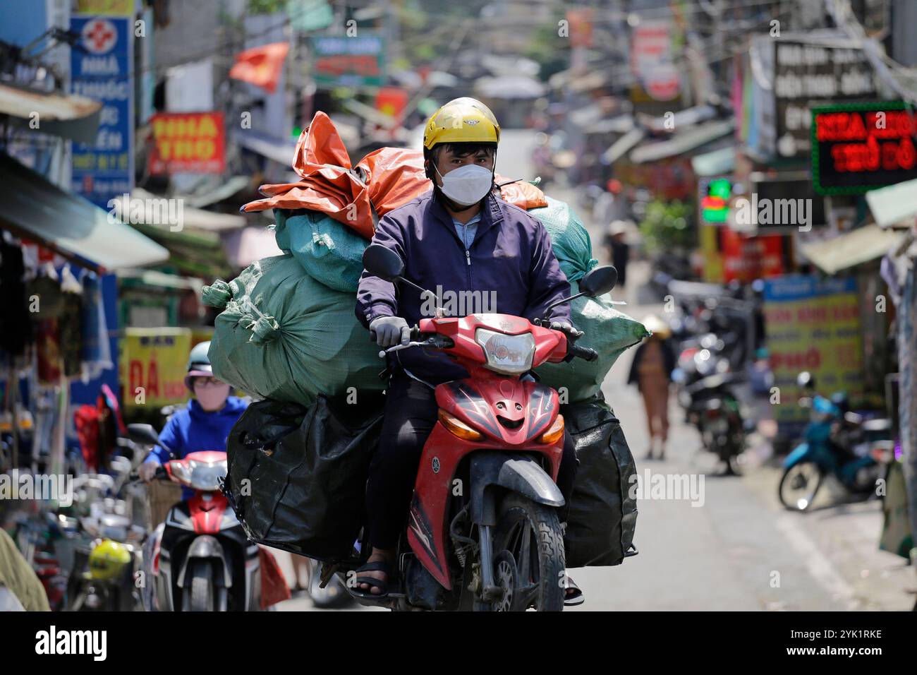 Hanoi, Vietnam - 2. Juli 2023: Motorradfahrer tragen eine Schutzmaske wegen schlechter Luftqualität, während er einen überladenen Roller fährt. Stockfoto