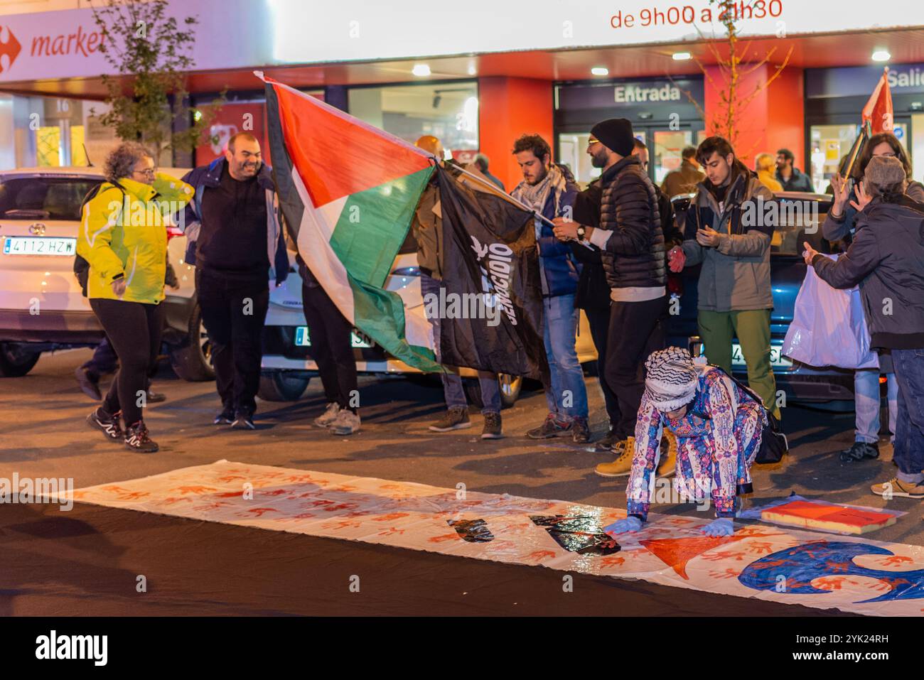 Logroño, La Rioja, Spanien. November 2024. Eine Gruppe von Aktivisten, die blaue Handschuhe tragen, nimmt an einer koordinierten künstlerischen Aktion auf einer Leinwand Teil, die auf dem Boden gespannt ist, während andere palästinensische Fahnen halten. Die Teilnehmer kombinieren Körperbewegungen als Teil der künstlerischen Performance, während einige Zuschauer die Handlung beobachten und dokumentieren. Die Leistung ist Teil einer größeren Demonstration zur Unterstützung Palästinas. Quelle: Mario Martija/Alamy Live News Stockfoto